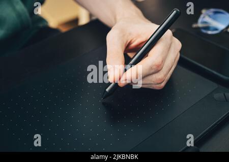 Young graphic designer man using  graphic tablet on black table at home office closeup. Stock Photo