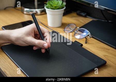 Young graphic designer man using graphic tablet on black table at home office closeup. Stock Photo