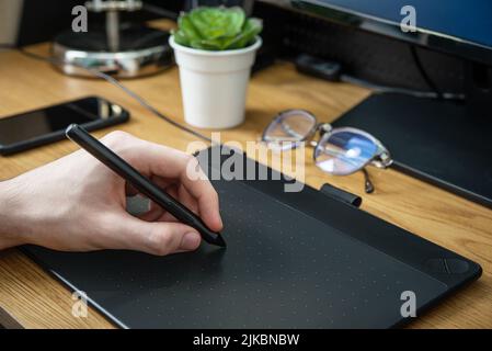 Young graphic designer man using graphic tablet on black table at home office closeup. Stock Photo