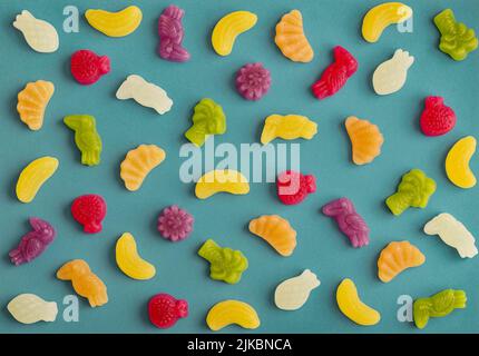 Jelly candies in shape of fruits, trees and birds as pattern on blue background Stock Photo