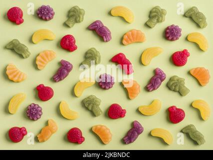 Jelly candies in shape of fruits, trees and birds as pattern on green background Stock Photo