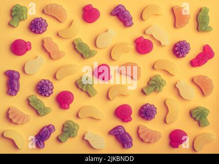 Jelly candies in shape of fruits, trees and birds as pattern on yellow background Stock Photo