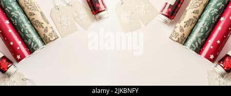 Rolls of colored wrapping paper with gift tags and  sparkle red confetti on white background, top view Stock Photo
