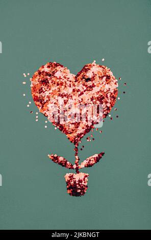 Red sparcling confetti in shape of heart on green background. Stock Photo