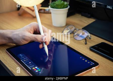 KIEV, UKRAINE - DECEMBER 21, 2021:Man with Apple Pencil using iPad Pro for drawing. iPad Pro was created and developed by the Apple inc. Stock Photo