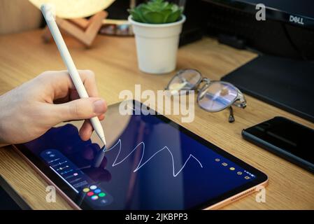 KIEV, UKRAINE - DECEMBER 21, 2021:Man with Apple Pencil using iPad Pro for drawing. iPad Pro was created and developed by the Apple inc. Stock Photo