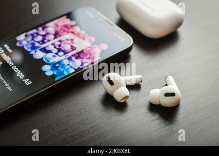 KIEV, UKRAINE - FEBRUARY 10, 2022:  Charging case and the new iPhone 13 Pro with Apple music app on screen next to New Apple Computers AirPods Pro hea Stock Photo