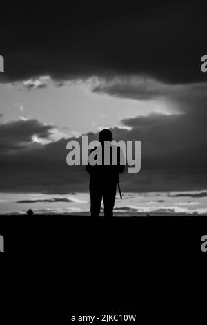 A silhouette of male standing on hill under night sky with admiring the Break in the clouds. Black and White Stock Photo