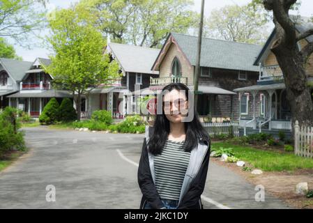 A chinese woman standing on a road through the national historic landmarks oak bluffs campground from the 19th century on martha's vineyard. Stock Photo