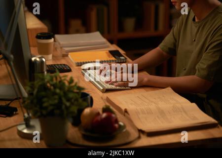 Hands of adult female student typing on computer keyboard while studying at home in the evening Stock Photo