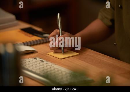 Close-up of hand making a note with pen on sticky paper Stock Photo