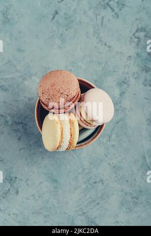 Colorful macarons in bowl on blue background, top view Stock Photo