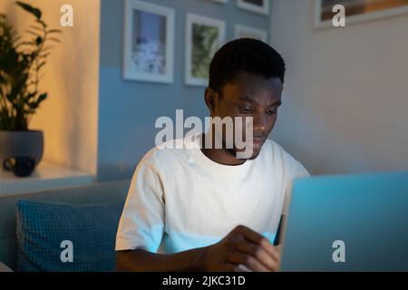 African American programmer writes code for website looking at screen of computer in room at night Stock Photo
