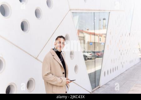 Young hispanic arab man smiling looking at camera using a smartphone in the street, social media and technology concepts Stock Photo