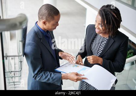 Cheerful team of white collar workers standing on staircase of modern office building and analyzing statistic data Stock Photo