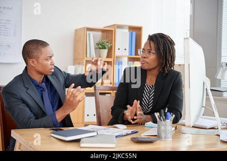 Group of creative interior designers in formalwear gathered together in spacious open plan office and brainstorming on their joint project Stock Photo