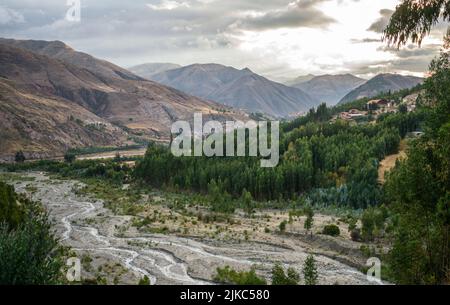 nearby forest with river and distant mountains, sunset in cloudy sky, urcospampa, cusco, peru Stock Photo