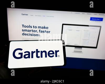 Person holding cellphone with logo of US research company Gartner Inc. on screen in front of business webpage. Focus on phone display. Stock Photo