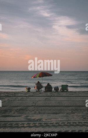 A couple resting on a sandy beach on the sunset Stock Photo