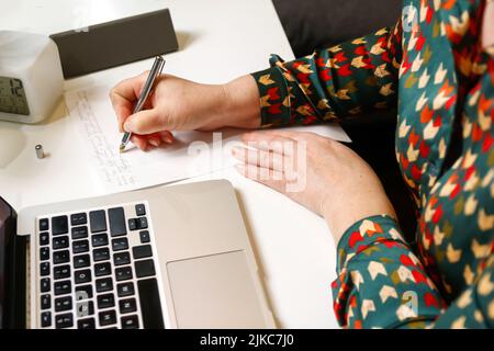 Defcous female hand writing by pen. Unrecognizable elegant woman working on computer at office. Start or finish of a work day. Workspace. Top view. Ti Stock Photo