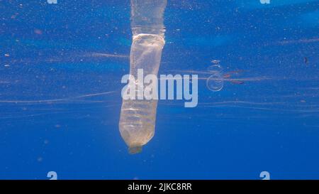 Plastic pollution, plastic bottle and cup in blue water. Discarded plastic bottle slowly drifting under surface of blue water in sunlight. Plastic gar Stock Photo