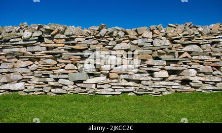 A colourful dry stone wall on a sunny day between a clear blue sky and green grass. Stock Photo