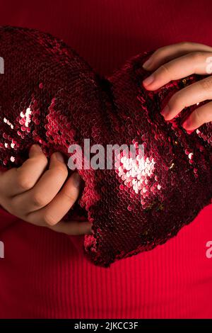 A vertical shot of female hands holding a heart-shaped red cushion Stock Photo