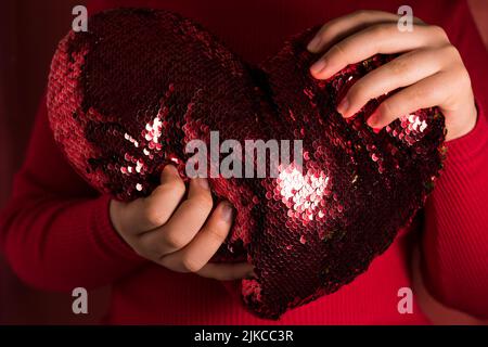 A closeup shot of female hands holding a heart-shaped red cushion Stock Photo