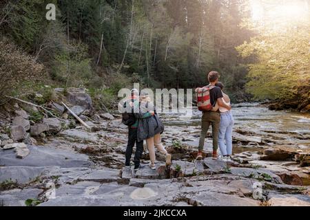 Rear on two couples standing and hugging at river on rocks. Hikers in mountains valley. Stock Photo