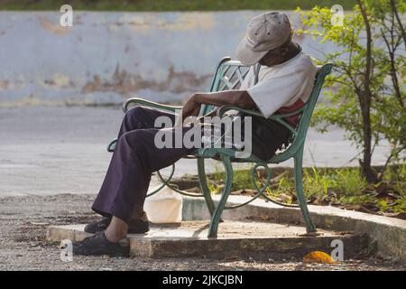 a closeup of a man sleeping sitting up on the outdoor bench in Matanzas, Cuba Stock Photo