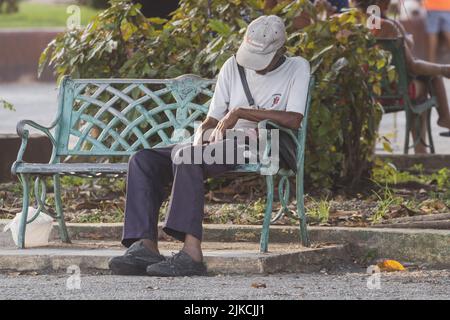 a closeup of a man sleeping sitting up on the outdoor bench in Matanzas, Cuba Stock Photo