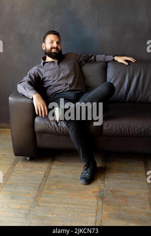 A man with a black beard is sitting on a leather sofa. businessman Stock Photo