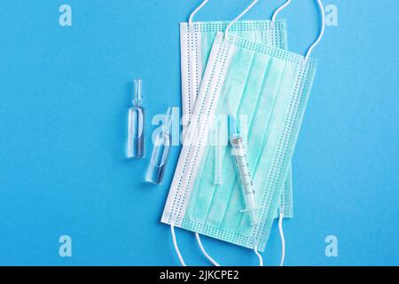 Sterile medicine background with injection ampoules, sharp needle and protective face masks on clean blue desk. Vaccination concept. Stock Photo