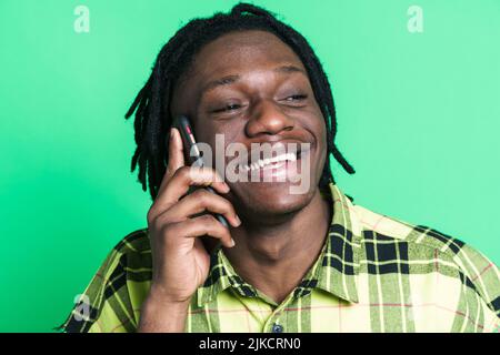Young black man with dreadlocks talking on mobile phone isolated over green background Stock Photo