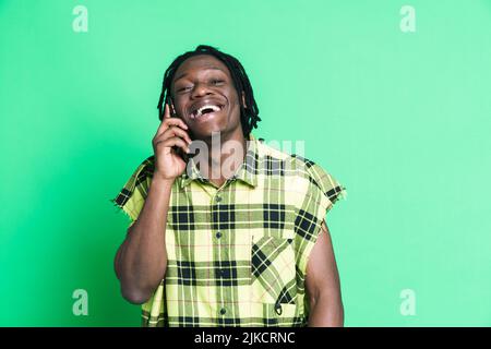 Young black man with dreadlocks talking on mobile phone isolated over green background Stock Photo