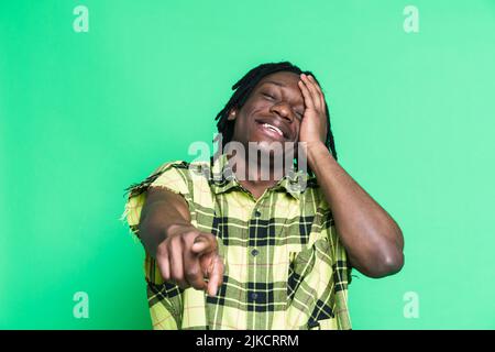 Young black man laughing and pointing finger at camera isolated over green background Stock Photo
