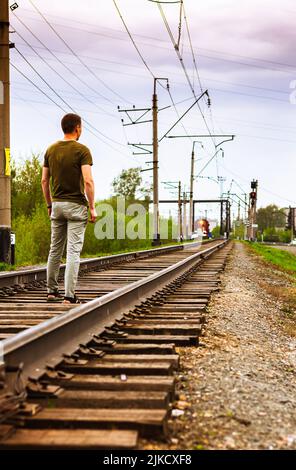 Man standing on train tracks On the Sunset in melancholy mood. Red light on coming train, selective focus. Man dreams of traveling, get out of city an Stock Photo