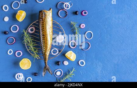 Smoked mackerel with rings of onion, lemon, olives, rosemary on blue background. Top view Stock Photo