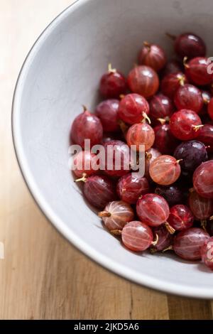 A bowl of freshly picked and washed homegrown Hinnonmaki Red gooseberries on a wooden chopping board. Stock Photo