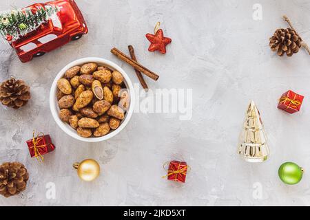 Candied or sugared almonds with honey and cinnamon in bowl on gray with Christmas decoration background. Traditional Christmas sweets for holidays. Top view, copy space Stock Photo