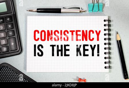 CONSISTENCY IS KEY text on paper sheet with chart, dice, spectacles, pen, laptop and blue and yellow push pin on wooden table - business, banking, fin Stock Photo