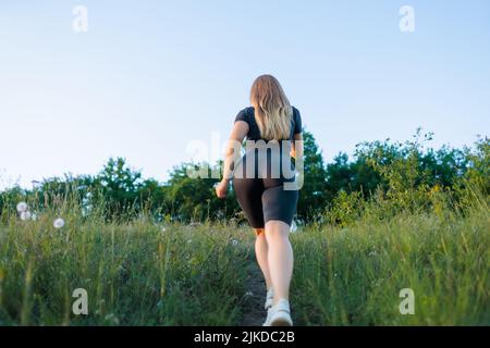 blonde in tight sports leggings climbs uphill along the path Stock Photo