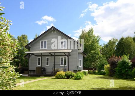 Contemporary two-story house of timber in countryside in summer with shrubs, green lawn and blooming trees. Russian dacha in Moscow region. Stock Photo