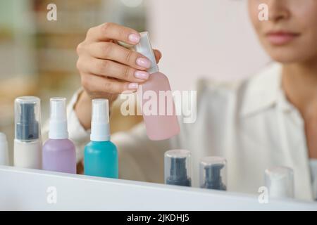 Hand of young woman holding plastic bottle with liquid self care product while standing in front of display with row of beautycare items Stock Photo