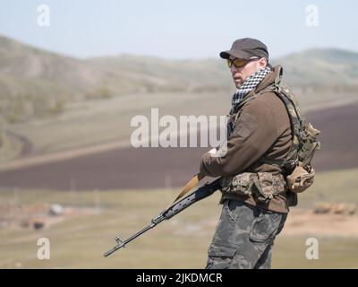 Mercenary sniper standing with a rifle and looking to the side. Armed conflict. Stock Photo
