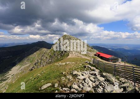 Chopok, Nizke Tatry, Low Tatras, Slovakia, Europe - mountain cabin and under top, peak and summit of the rocky mountain. Hikers on the top of hill. Wi Stock Photo