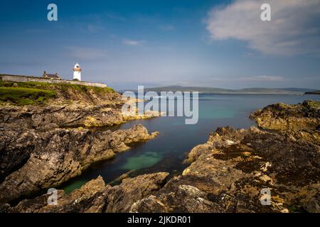 rocky shoreline with turquoise pools and the historic Broadhaven Lighthouse on a clifftop promontory at the entrance of Broadhaven Bay Stock Photo