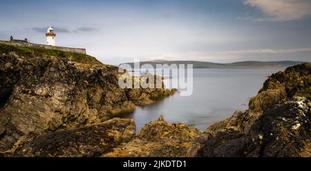 rocky shoreline with turquoise pools and the historic Broadhaven Lighthouse on a clifftop promontory at the entrance of Broadhaven Bay Stock Photo