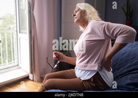 Senior caucasian woman holding her lower back, suffering from pain. Stock Photo