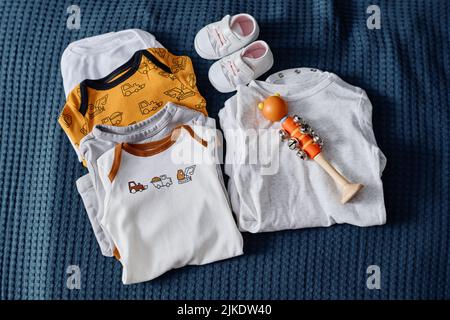 Collection of new casualwear for future baby, tiny white leather shoes and toy on blue textile background or bed with velvet cover Stock Photo